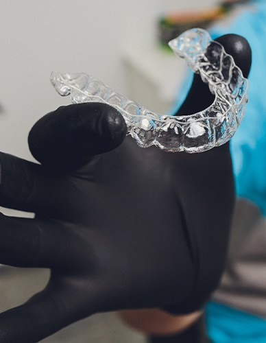 Dentist with black gloves holding clear aligner