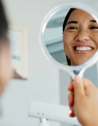 Woman smiling at reflection in handheld mirror