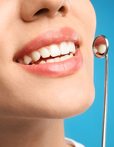 Nose-to-chin view of a woman smiling holding dental mirror to teeth with blue background