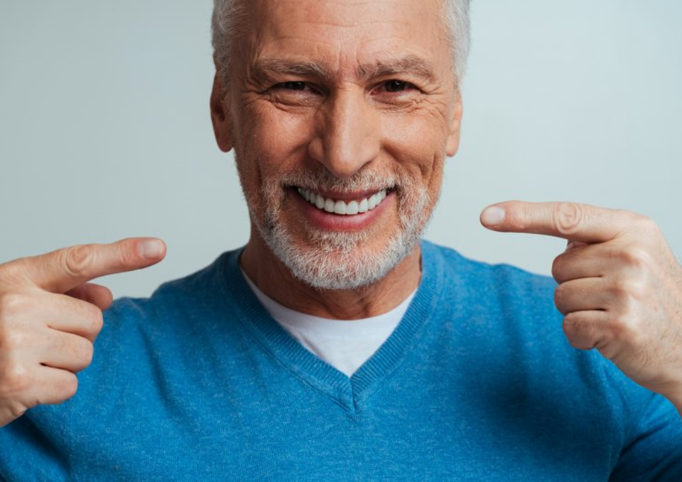 a man with dental crowns pointing at his smile