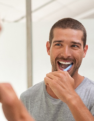 Man smiling while brushing his teeth in bathroom