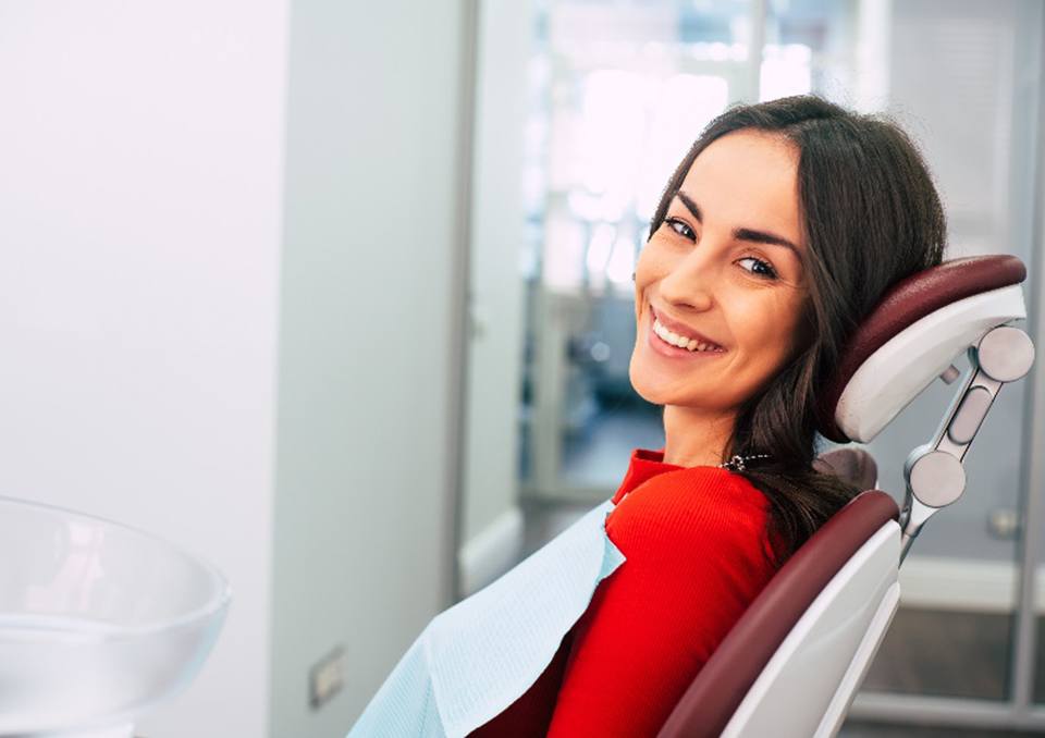 Woman in red shirt smiling while sitting in dental chair
