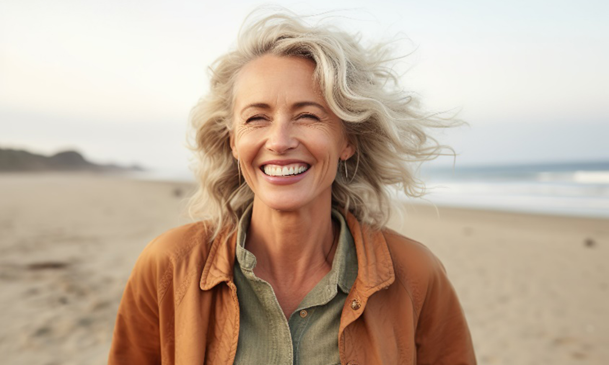 Mature woman in brown jacket smiling while walking on beach