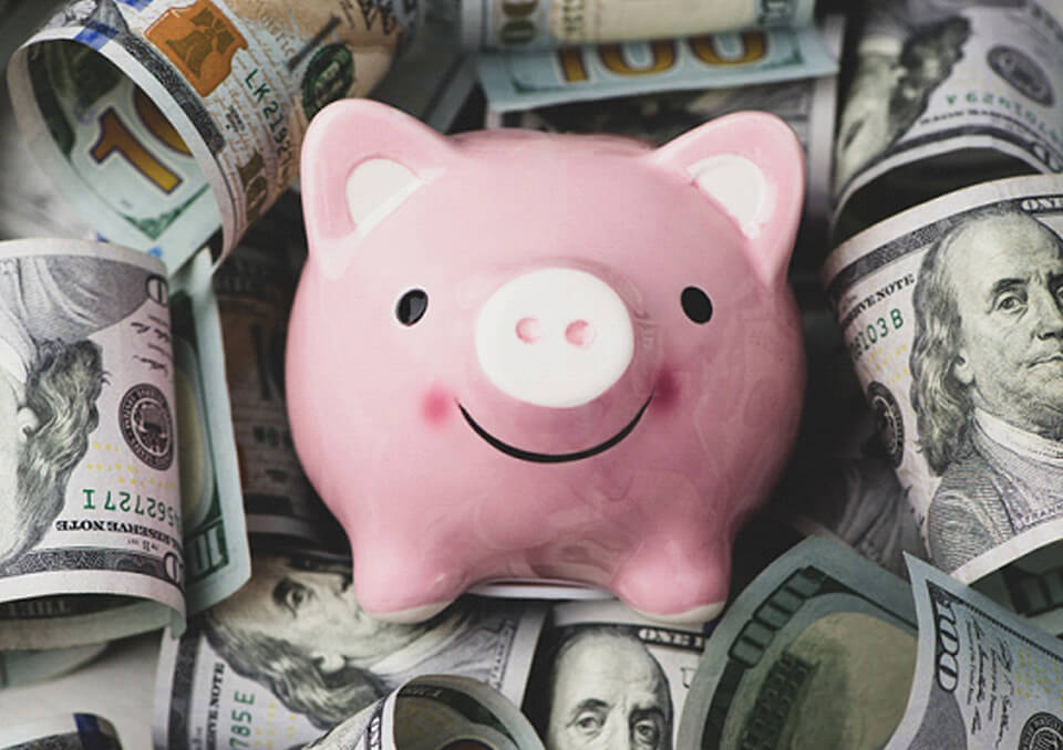 Pink piggy bank laying on top of a pile of dollar bills