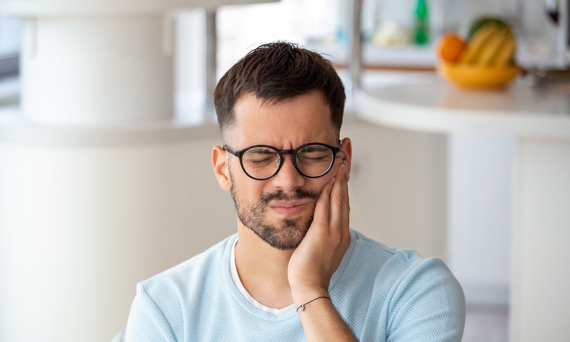 Man with glasses rubbing his jaw in pain