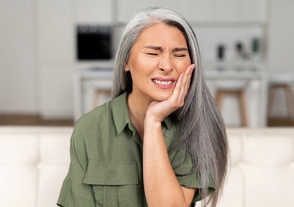 Woman sitting on couch rubbing jaw in pain