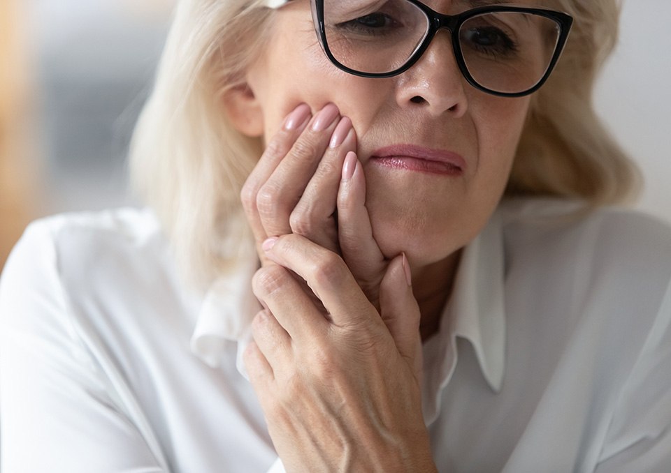 Senior woman with glasses rubbing jaw in pain