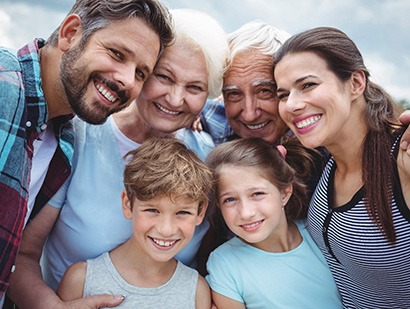 Three generations of a family smiling outdoors while wearing backpacks