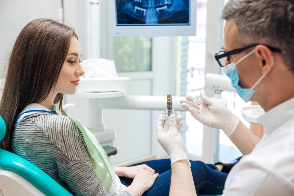 Dentist showing woman in dental chair a sample implant