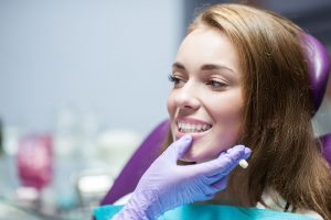 Woman with brown hair smiling at dentist who is touching her jaw with a gloved hand