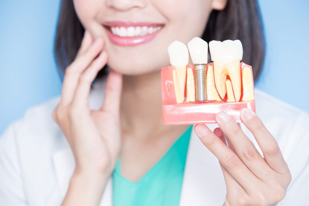 Nose-to-chest view of dentist holding sample implant in one hand and touching her cheek with the other