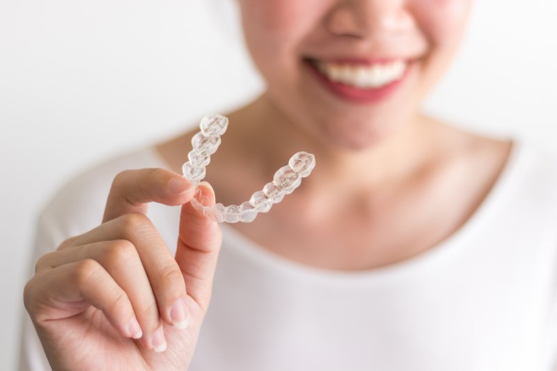 person holding Invisalign aligner and smiling