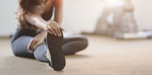 Woman in gym clothes sitting on floor stretching her leg